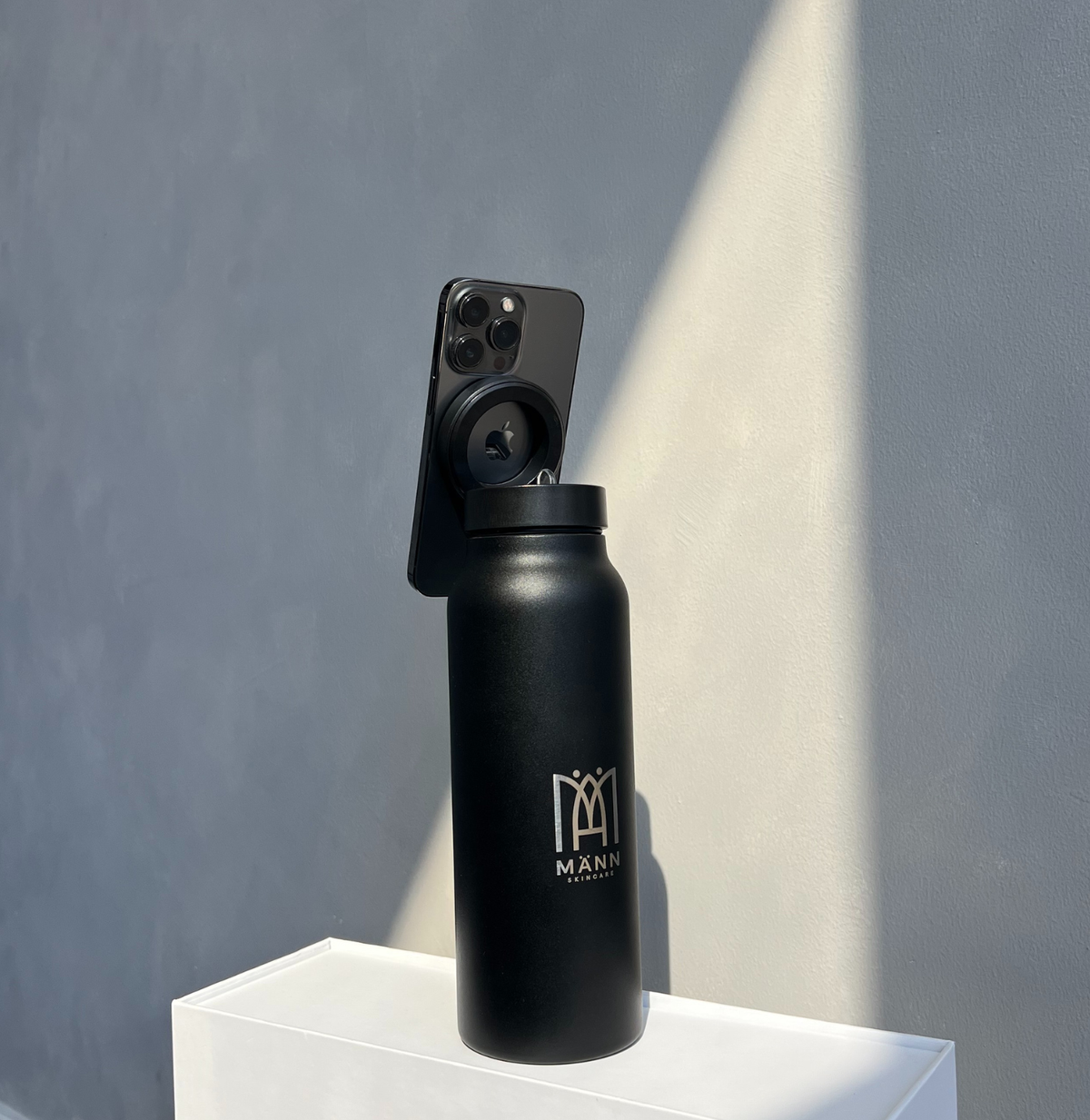 Black water bottle with a phone on top against a gray wall