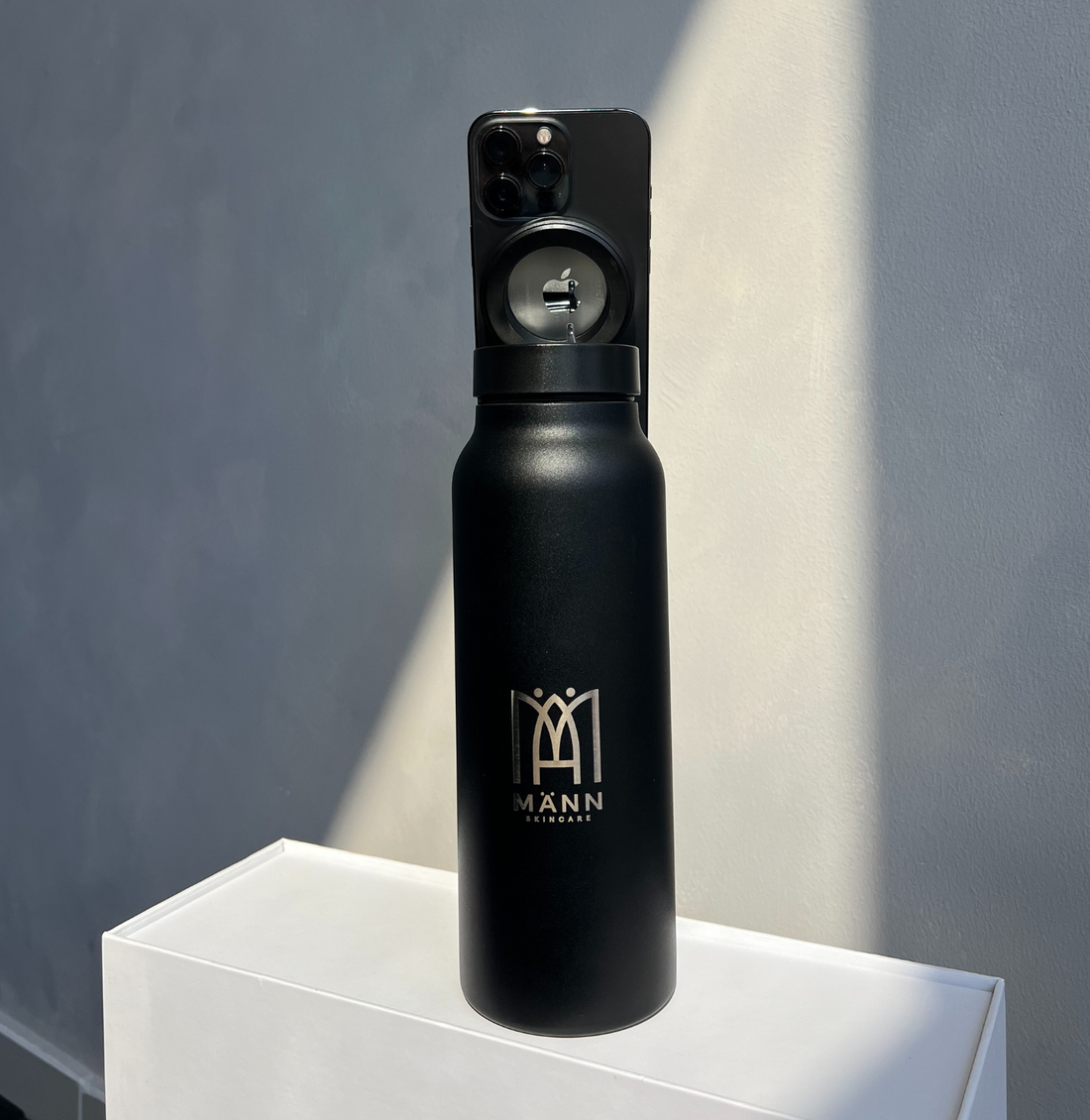 Black spray bottle with a brand logo on a white platform against a gray background